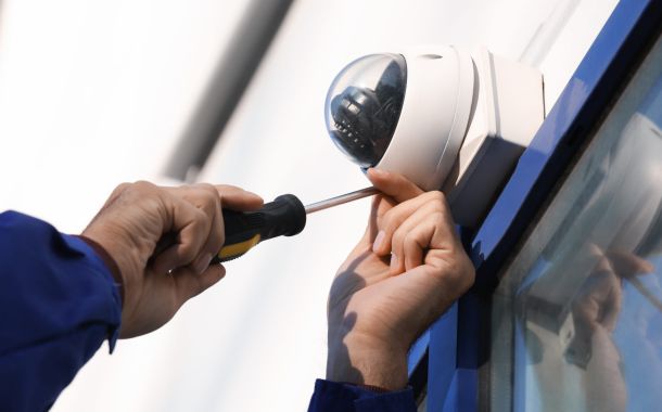Tecnico che installa una telecamera a circuito chiuso su una parete all'aperto, primo piano